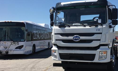 A white zero emission bus is parked next to a white BYD electric truck