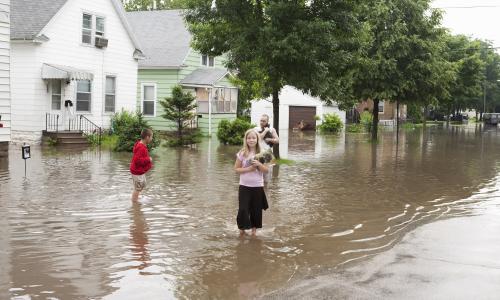 A family stands in ankle deep water holding some of their belongings. 