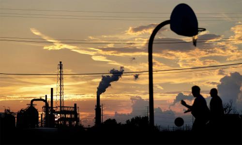 People playing basketball at dusk with a refinery in the distance