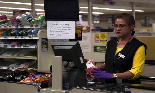 A cashier during the COVID-19 crisis, with food scarcity signs.