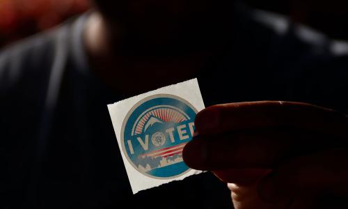 Person holding a sticker that reads "I voted."