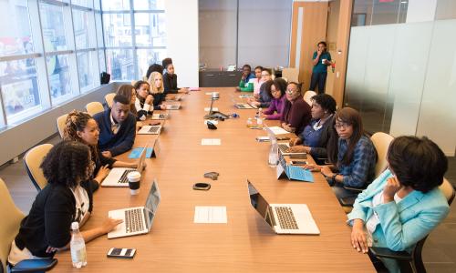 Many people sit around a table in a meeting room.