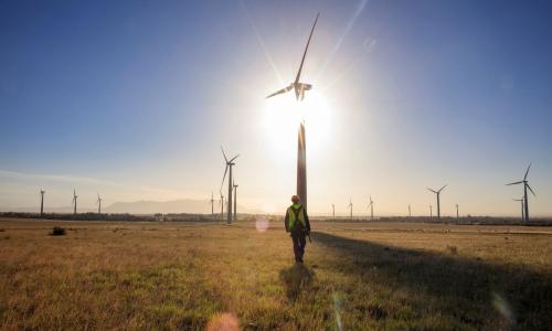 Worker walks toward a wind turbine at sunset.