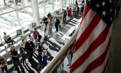 people waiting in line at a polling place, with an American flag in the foreground