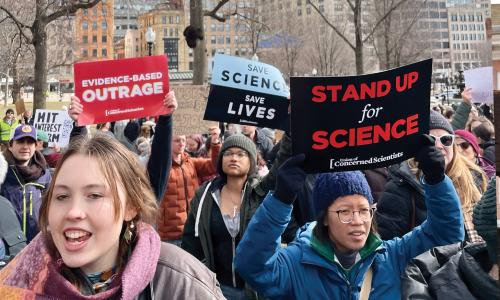 Protesters with signs saying, "Evidence-Based Outrage" and "Stand Up for Science"