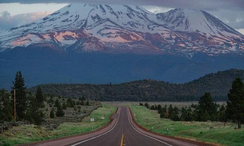 A road leading to a snow capped mountain.