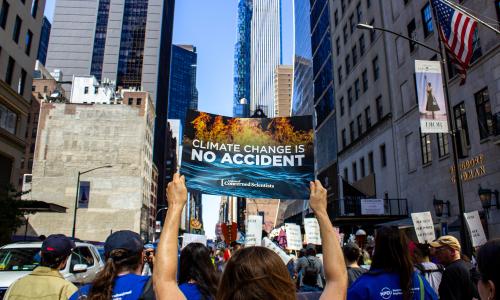 A person in a crowd at a rally holding a sign that reads "Climate change is no accident."