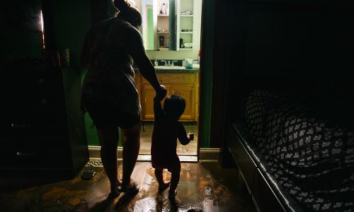 A parent and child walk through their flooded house.