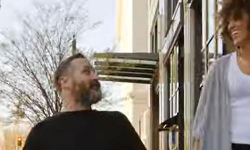 a man in a wheel chair and a woman talking on a city sidewalk