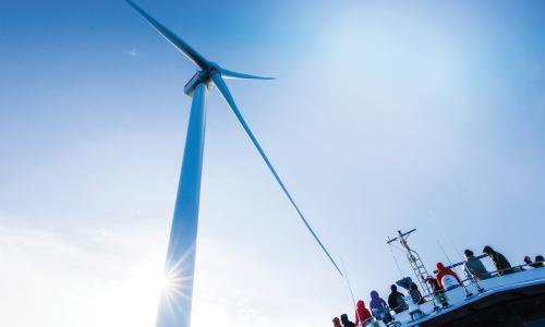 People on a boat riding past an offshore wind turbine.