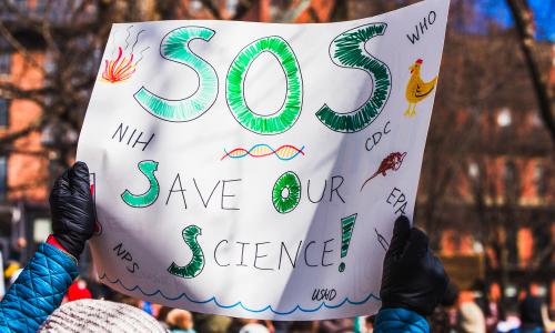 A sign that reads "SOS Save Our Science."